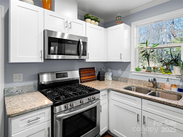 kitchen with light stone counters, a sink, white cabinets, ornamental molding, and appliances with stainless steel finishes