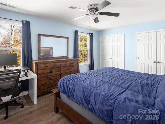 bedroom with two closets, wood finished floors, visible vents, and a ceiling fan