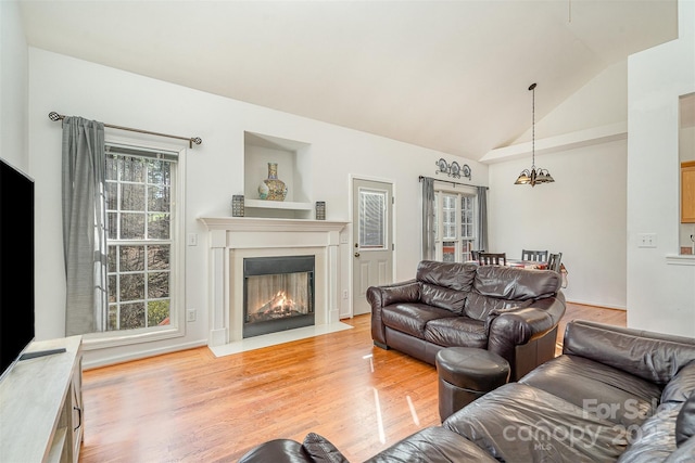 living room with a notable chandelier, a fireplace with flush hearth, light wood-type flooring, and vaulted ceiling