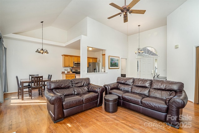 living room with light wood-style flooring, ceiling fan with notable chandelier, and high vaulted ceiling