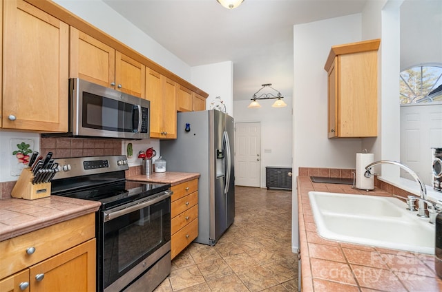 kitchen with a sink, stainless steel appliances, decorative backsplash, and tile counters