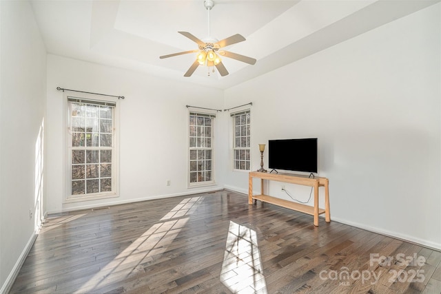 living area with ceiling fan, a raised ceiling, baseboards, and hardwood / wood-style flooring