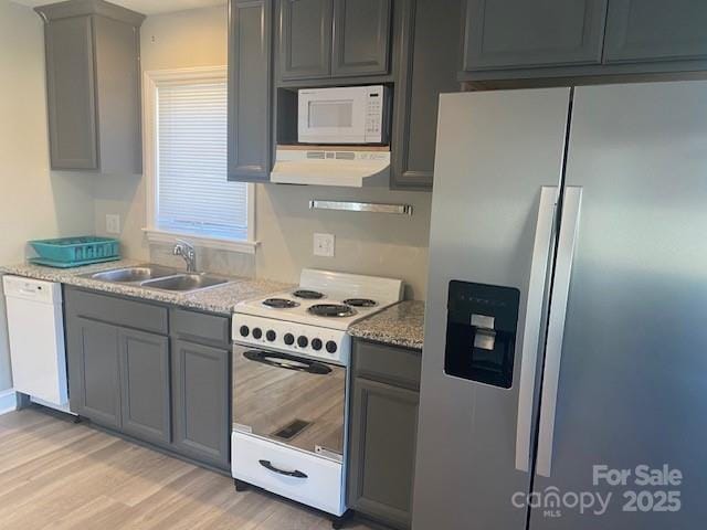 kitchen with gray cabinetry, light wood-type flooring, exhaust hood, white appliances, and a sink