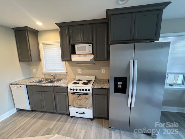 kitchen with light wood finished floors, white appliances, baseboards, and a sink