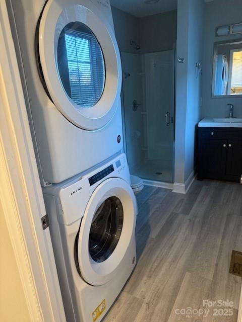 laundry area with a sink, light wood finished floors, stacked washer / dryer, baseboards, and laundry area