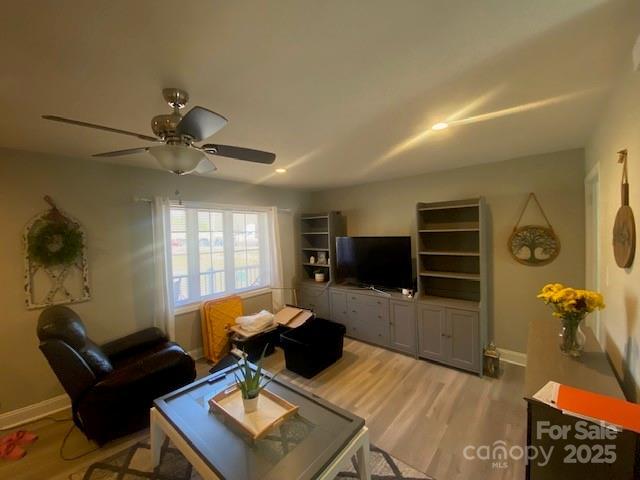 living room with wood finished floors, a ceiling fan, and baseboards