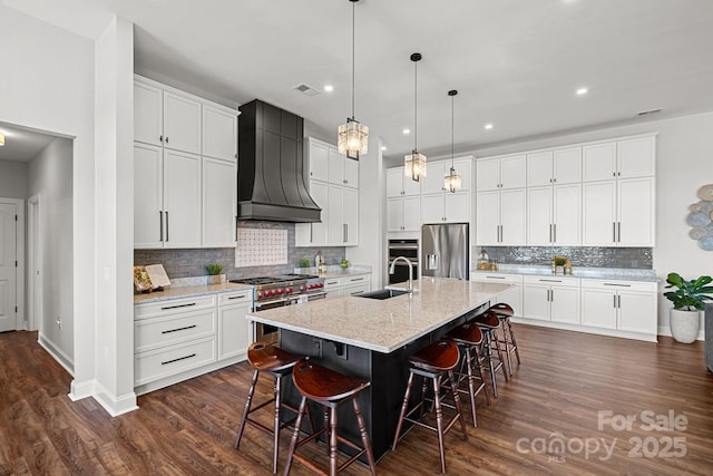 kitchen with custom range hood, appliances with stainless steel finishes, a kitchen breakfast bar, and a sink