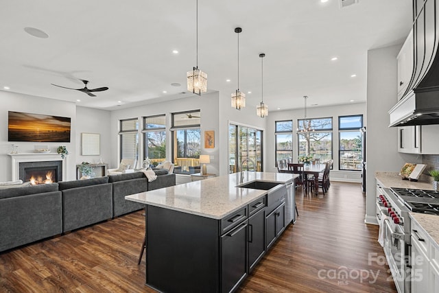 kitchen featuring high end range, dark wood-type flooring, open floor plan, light stone countertops, and a sink