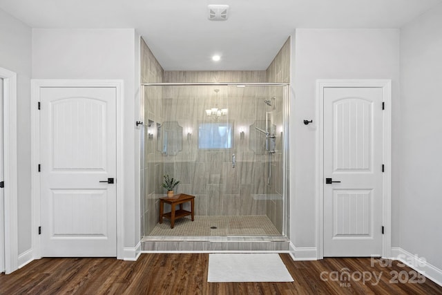 bathroom with a chandelier, a stall shower, baseboards, and wood finished floors