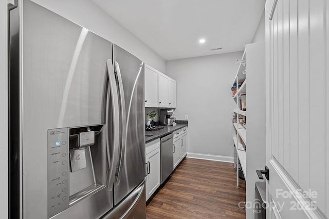 kitchen featuring dark wood-style flooring, dark countertops, appliances with stainless steel finishes, white cabinets, and baseboards