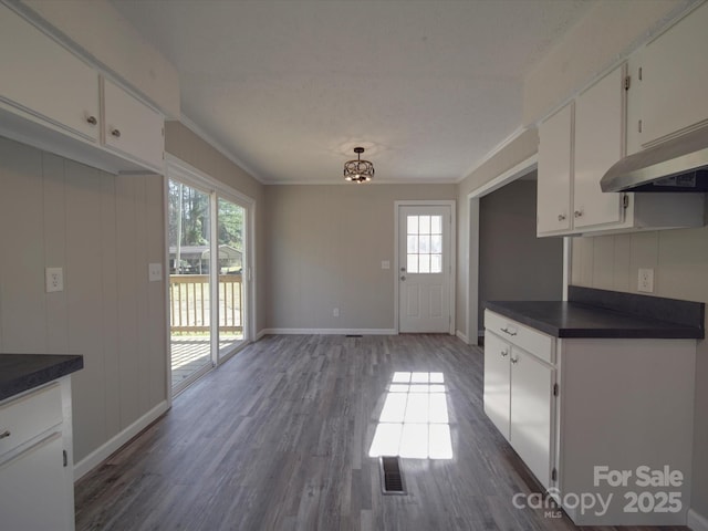 kitchen featuring white cabinetry, baseboards, ornamental molding, dark countertops, and dark wood finished floors