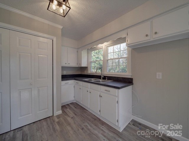 kitchen featuring dark countertops, white cabinets, a sink, a textured ceiling, and wood finished floors