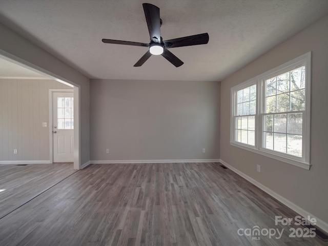 empty room with a textured ceiling, baseboards, and wood finished floors