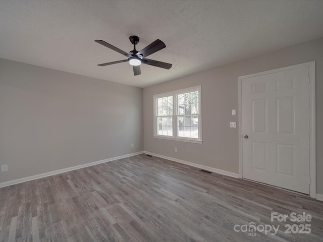 spare room with visible vents, ceiling fan, a textured ceiling, wood finished floors, and baseboards