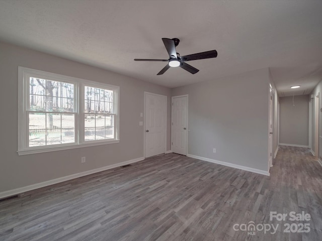 unfurnished room with visible vents, attic access, ceiling fan, wood finished floors, and baseboards