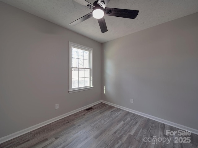 unfurnished room with visible vents, a textured ceiling, baseboards, and wood finished floors