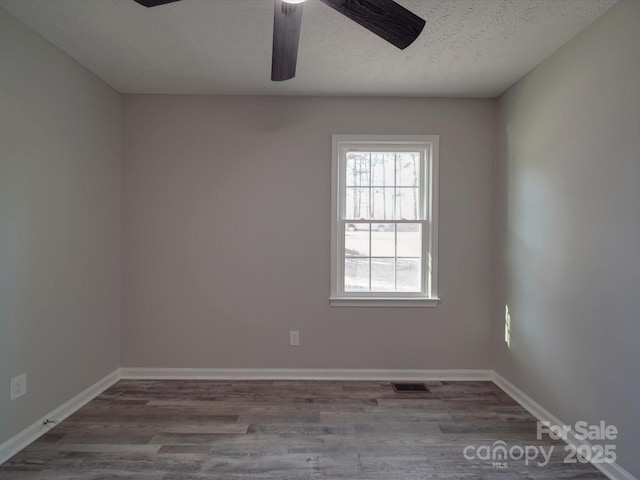 empty room featuring visible vents, a textured ceiling, baseboards, and wood finished floors