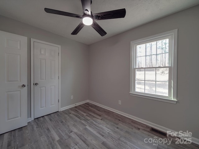 unfurnished bedroom with wood finished floors, visible vents, baseboards, and multiple windows