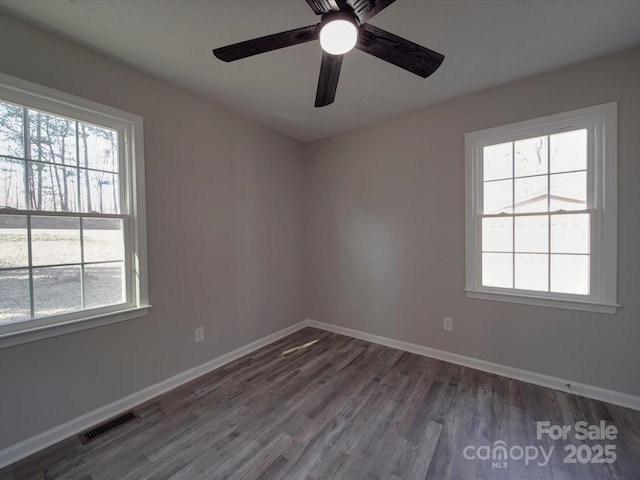 empty room featuring plenty of natural light, wood finished floors, visible vents, and baseboards