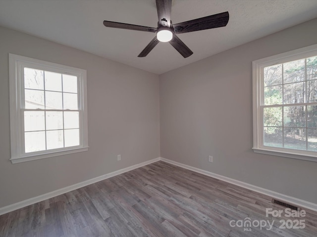 spare room with visible vents, plenty of natural light, baseboards, and wood finished floors