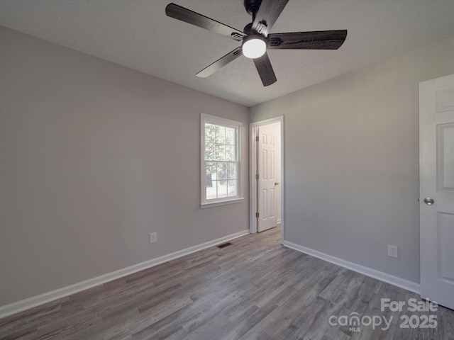 unfurnished room with a textured ceiling, ceiling fan, wood finished floors, visible vents, and baseboards