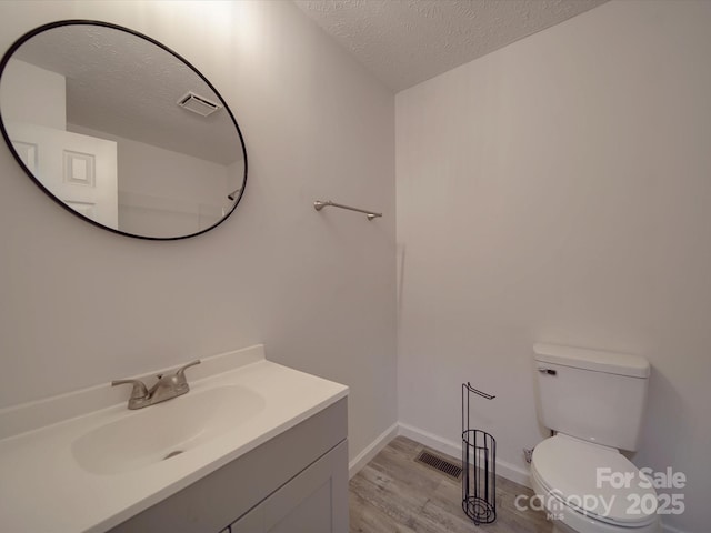 bathroom featuring visible vents, toilet, a textured ceiling, vanity, and wood finished floors