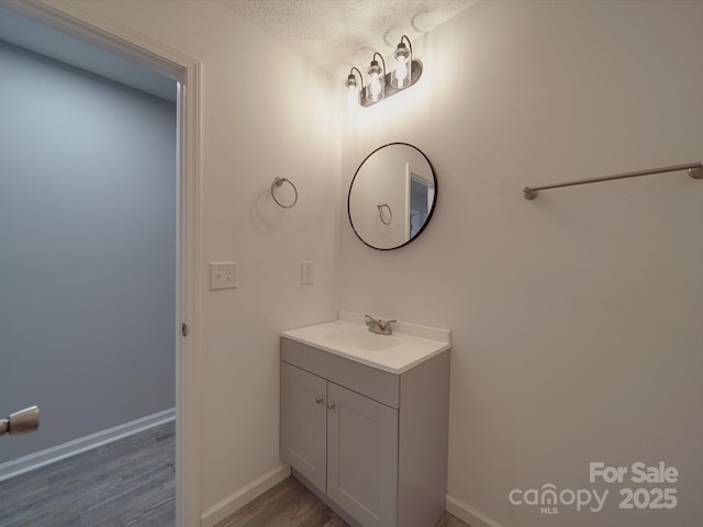 bathroom featuring baseboards, wood finished floors, a textured ceiling, and vanity