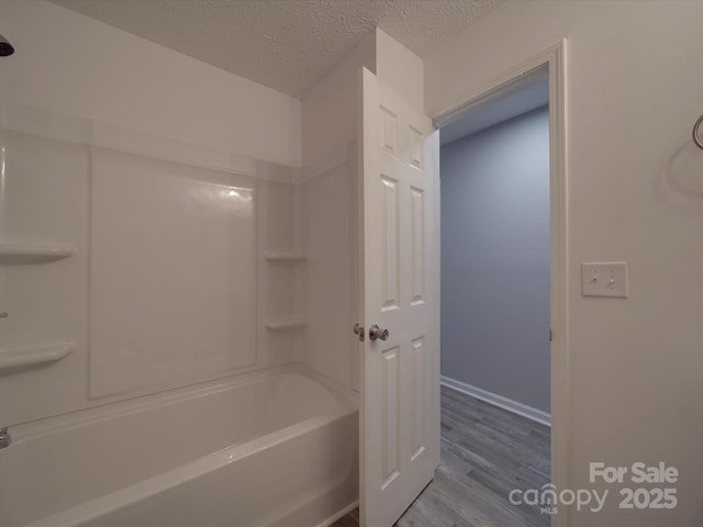 bathroom featuring a textured ceiling, shower / bathing tub combination, wood finished floors, and baseboards