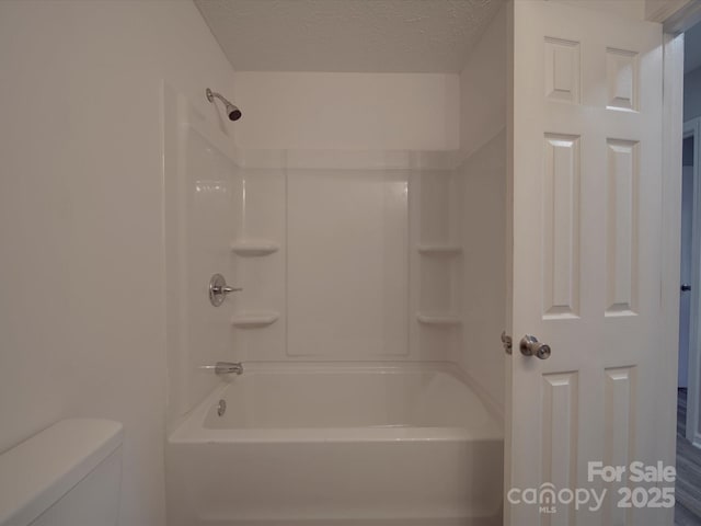 bathroom with a textured ceiling, washtub / shower combination, and toilet