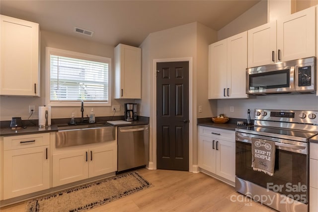 kitchen featuring light wood finished floors, stainless steel appliances, dark countertops, visible vents, and a sink