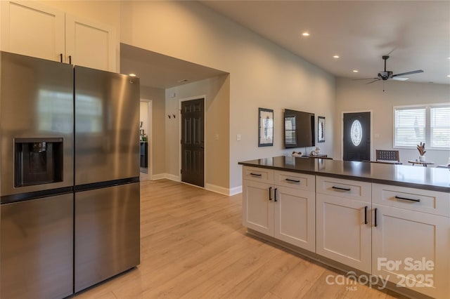 kitchen with dark countertops, white cabinetry, vaulted ceiling, light wood-type flooring, and stainless steel fridge with ice dispenser