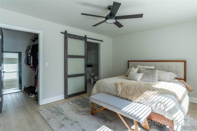 bedroom with a barn door, a spacious closet, baseboards, and light wood-style flooring