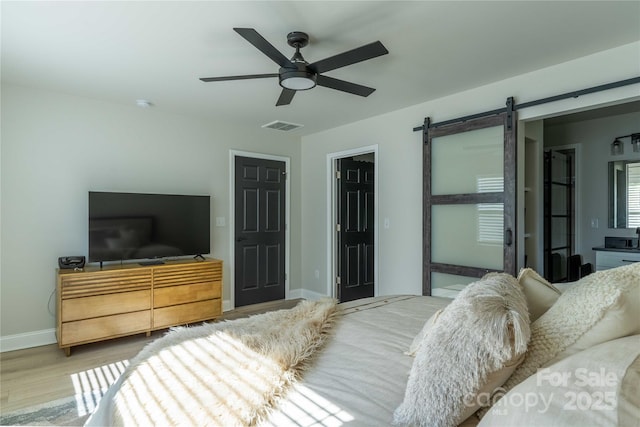 bedroom with visible vents, a barn door, a ceiling fan, wood finished floors, and baseboards