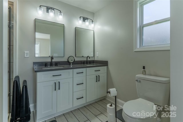 full bath featuring double vanity, a sink, toilet, and wood finished floors