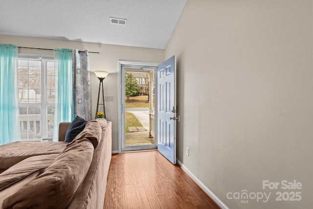 doorway with baseboards, a textured ceiling, visible vents, and wood finished floors