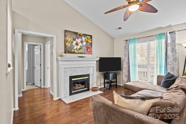 living room featuring visible vents, a premium fireplace, vaulted ceiling, wood finished floors, and baseboards