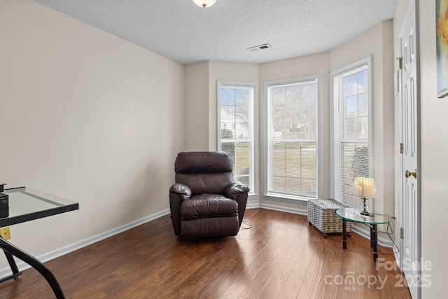 living area featuring a wealth of natural light, a textured ceiling, baseboards, and wood finished floors