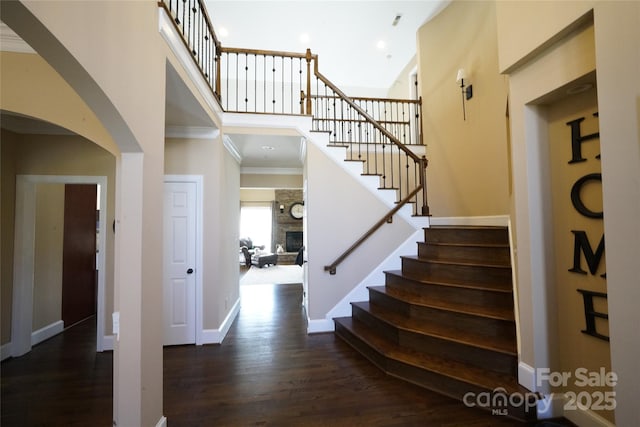 entrance foyer featuring baseboards, a towering ceiling, wood finished floors, crown molding, and a fireplace