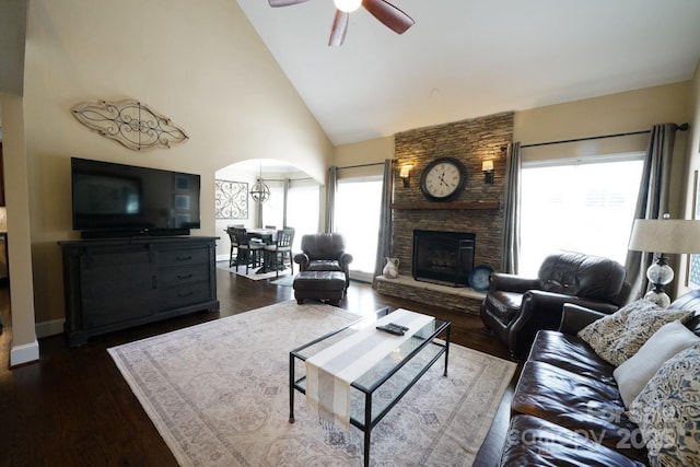 living area featuring arched walkways, a ceiling fan, dark wood-type flooring, a stone fireplace, and high vaulted ceiling