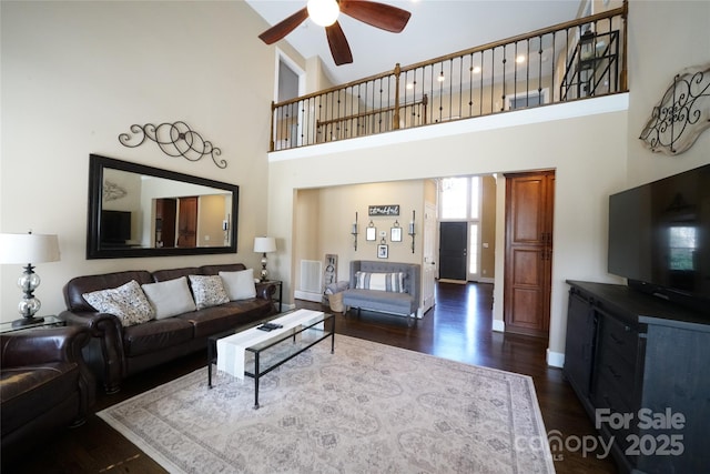 living room with a towering ceiling, dark wood-style floors, ceiling fan, and visible vents