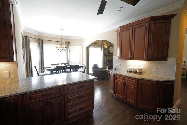 kitchen featuring arched walkways, a ceiling fan, light stone countertops, dark wood-style floors, and decorative light fixtures