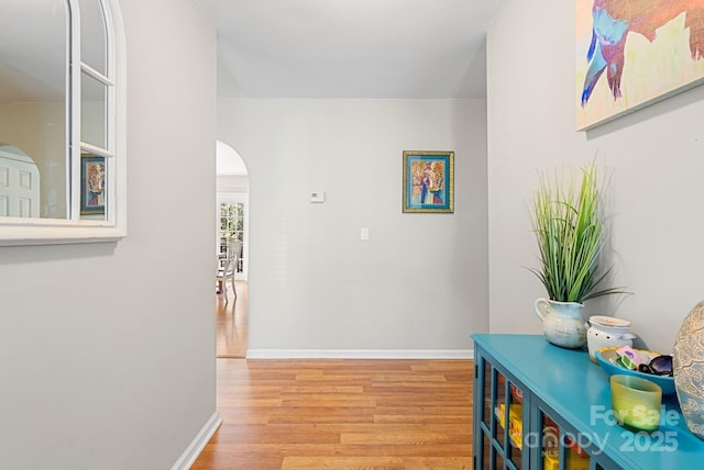 corridor with arched walkways, wood finished floors, and baseboards