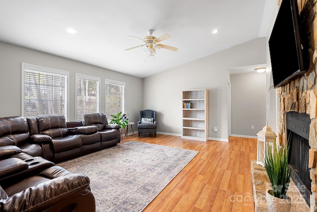 living room featuring baseboards, a fireplace with raised hearth, a ceiling fan, lofted ceiling, and light wood-style floors