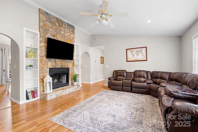 living room featuring arched walkways, vaulted ceiling, a fireplace, and wood finished floors