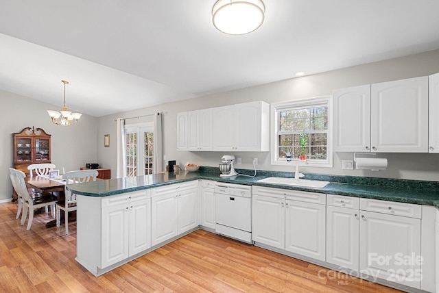 kitchen with dark countertops, a sink, light wood-type flooring, dishwasher, and a peninsula