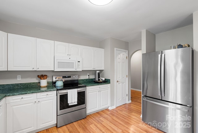 kitchen with arched walkways, appliances with stainless steel finishes, dark countertops, and white cabinets