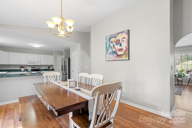 dining area with arched walkways, an inviting chandelier, light wood-style flooring, and baseboards