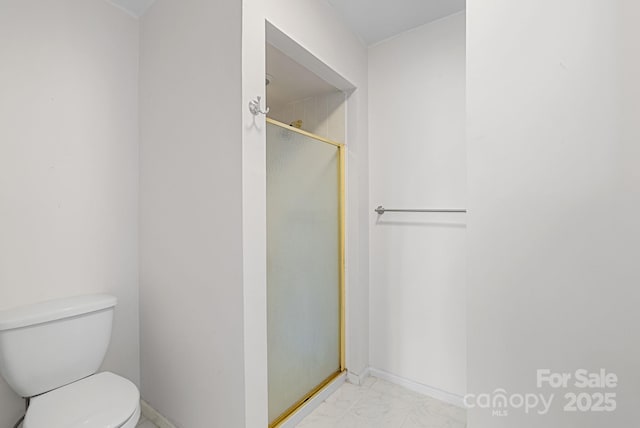 bathroom featuring toilet, marble finish floor, and a shower stall