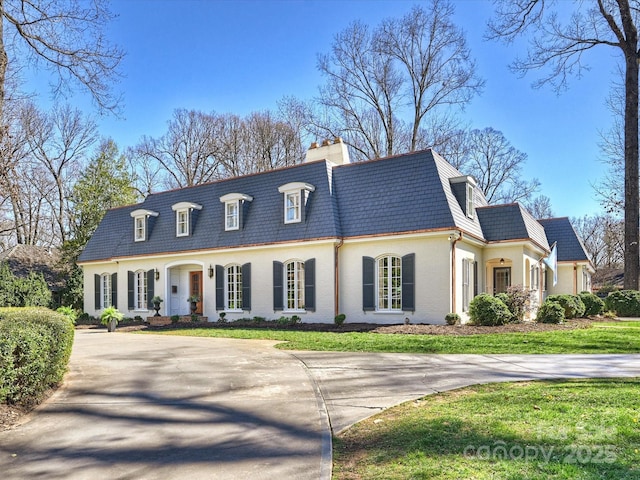 view of front facade featuring a chimney, mansard roof, concrete driveway, a high end roof, and a front lawn