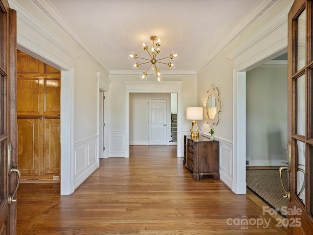 entryway with wainscoting, light wood-style flooring, ornamental molding, a decorative wall, and a notable chandelier